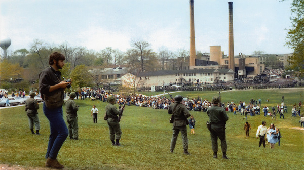 John Filo (left) with a camera in hand, overlooking the National Guardsmen and students on May 4, 1970. Photograph by James Coon, Kent State Shootings Photographs from Various Sources.  Citation: “Photographs: Kent State University, by Coon,” Kent State University Libraries. Special Collections and Archives, accessed May 4, 2024, http://omeka.library.kent.edu/special-collections/items/show/8721. 