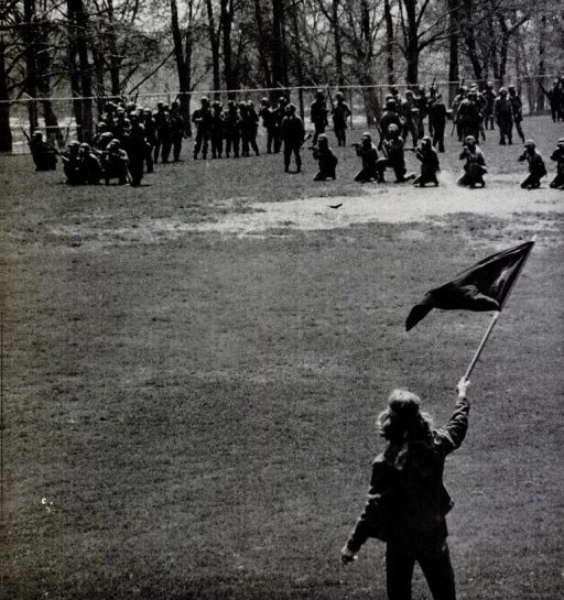 Surviving Kent State shooting victim Alan Canfora waving a flag before the Ohio National Guard, as pictured in the 15 May 1970 edition of LIFE magazine. Direct link here  Photo by John Filo, Photojournalism ‘72  Wikimedia, public domain